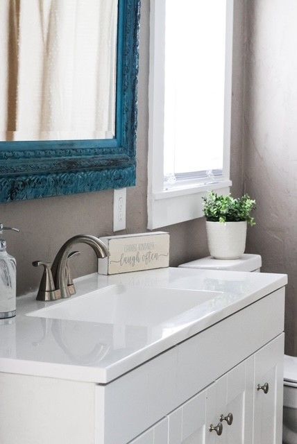 White bathroom vanity with a blue framed mirror, a small plant, and a window.