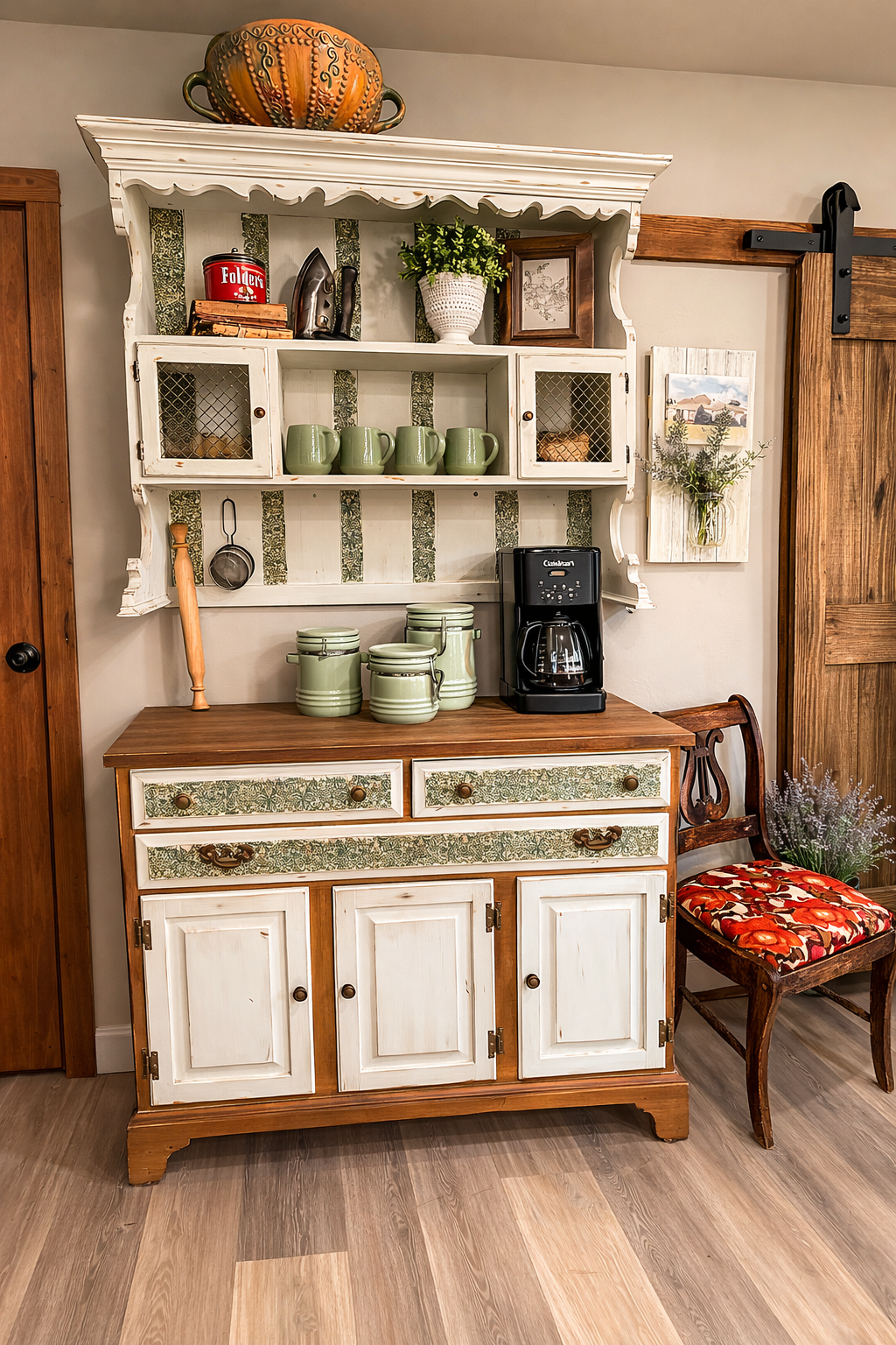 Rustic white hutch with shelves, dishes, plants, and coffee maker beside a wooden chair and barn door
