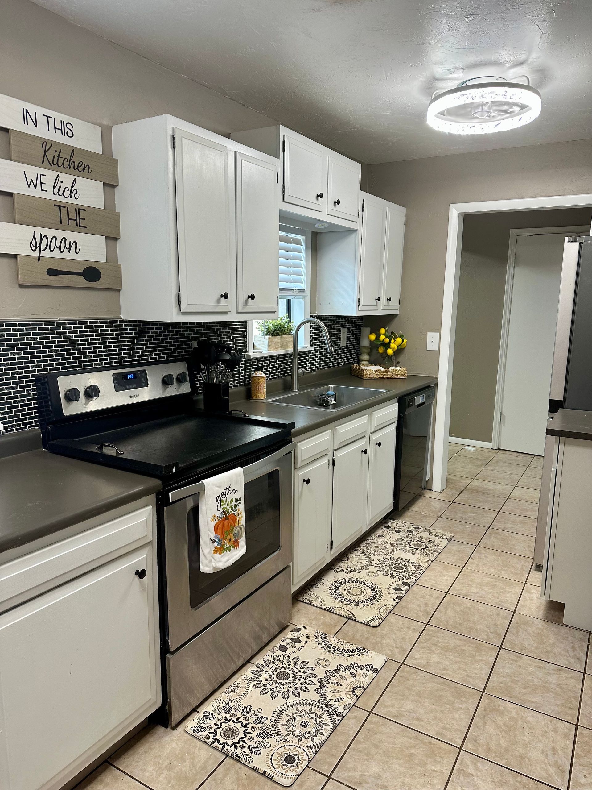 White kitchen cabinets with stainless steel appliances, dark countertops, patterned backsplash, beige floors.