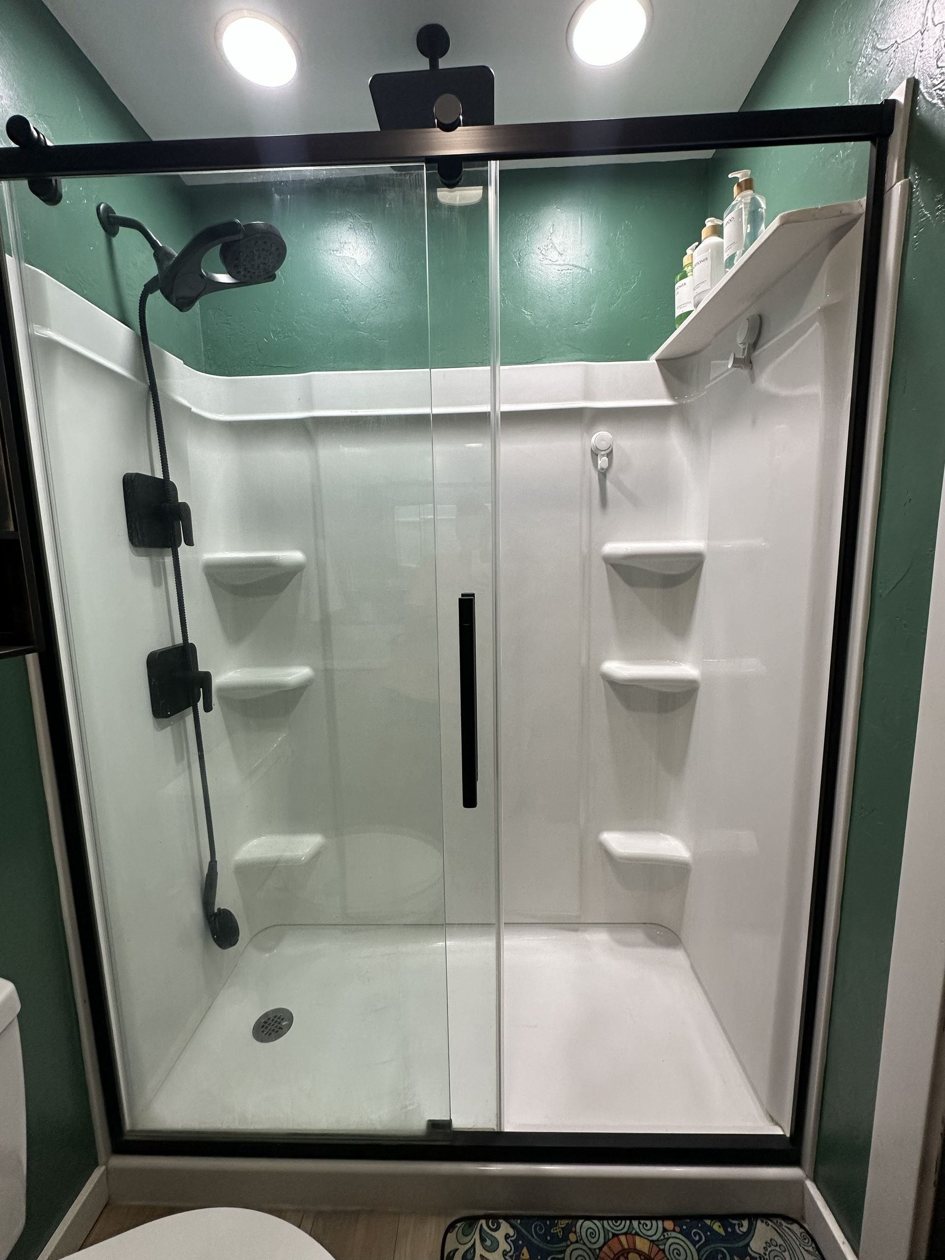 Shower stall with black frame, glass doors, and white interior against a green wall.