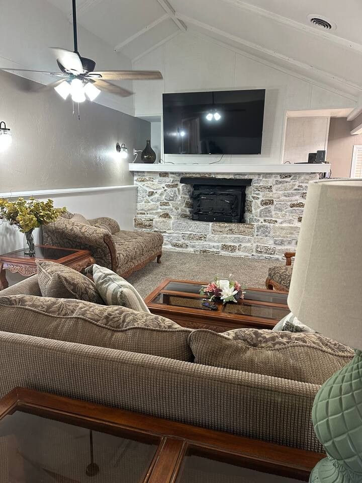 Living room with stone fireplace, TV, brown furniture, and a ceiling fan.