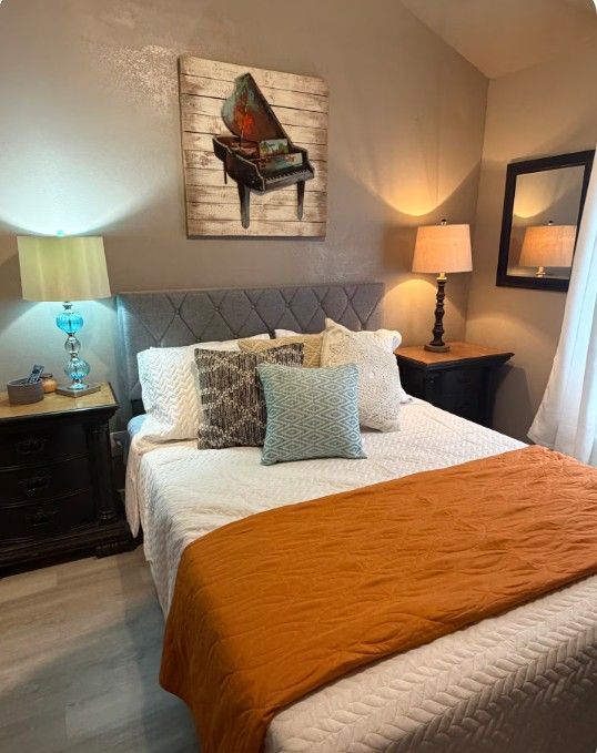 Cozy bedroom with bed, orange blanket, bedside lamps, mirror, and butterfly wall art