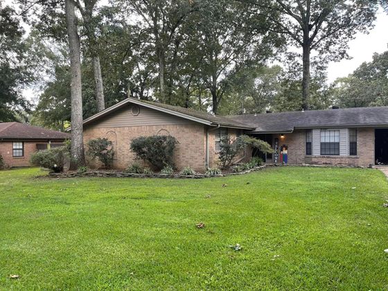 Single-story brick house with a large front lawn and tall trees in the yard