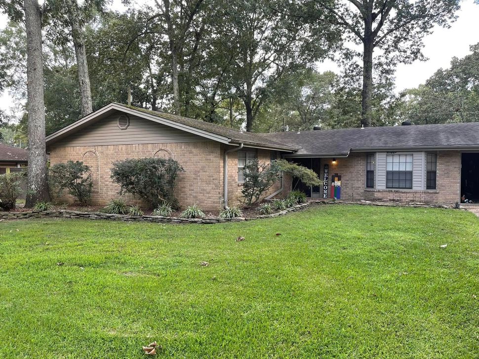 Brick single-story house with blue shutters and a wide green lawn under trees
