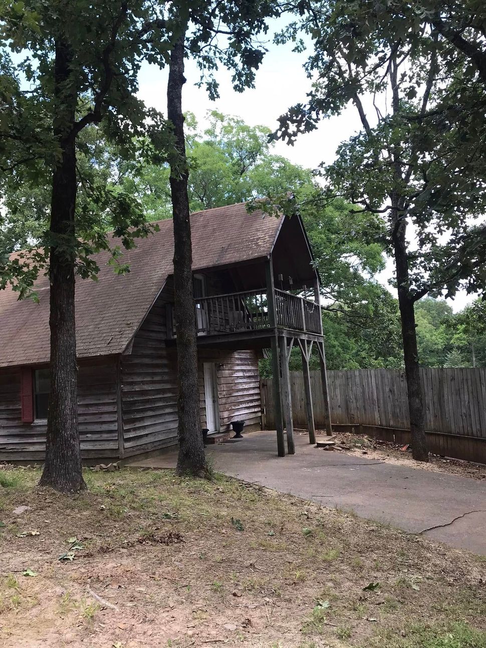 Wooden gatehouse and fence in a wooded park, with a paved path and a person in the doorway