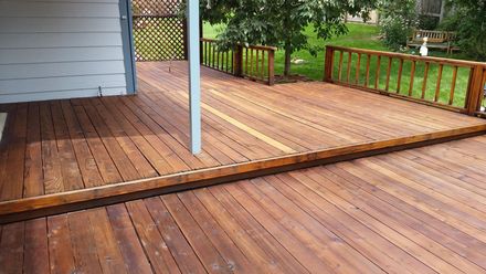 Wooden deck and patio with white support post beside a house, overlooking a fenced yard.
