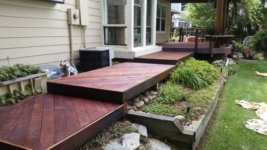 Wooden stepped deck beside a house, with a small garden and lawn in the yard.