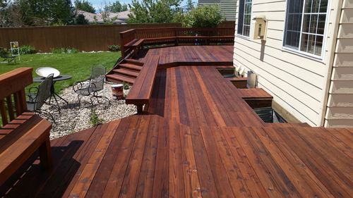 Wooden backyard deck with built-in benches beside a house and a grassy yard