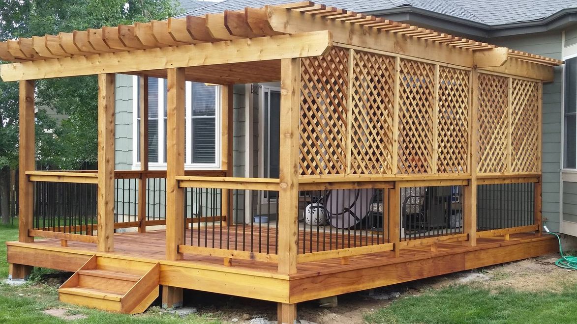 Wooden gazebo-style patio deck with lattice panels and a slatted roof in a grassy yard