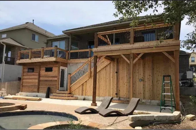 Backyard with a wooden deck, exterior staircase, and poolside loungers under construction