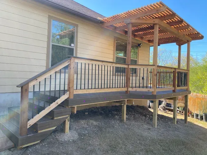 Wooden deck and stairs attached to a beige house, with a pergola-style roof and railing.