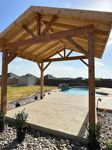 Wooden poolside pavilion with a pitched roof beside a backyard swimming pool under a blue sky