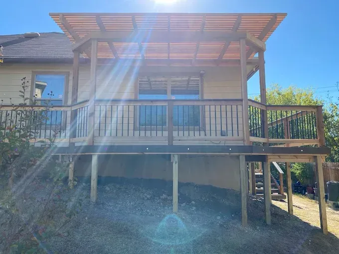 Sunlit wooden house deck with railing and stairs on a grassy slope