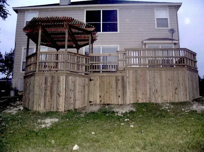 Back deck with wooden pergola and railing on the rear of a beige house