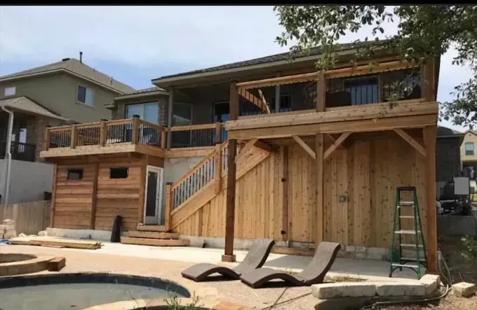 Wooden two-story house with a deck and stairs beside a backyard pool area