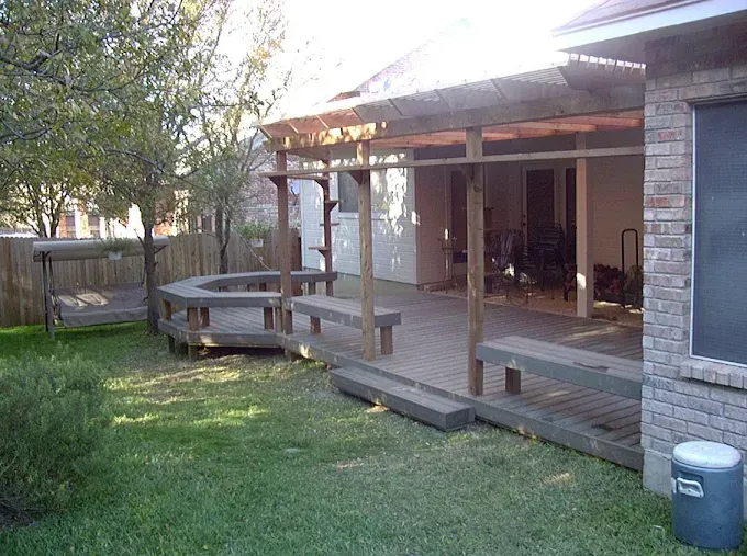 Backyard patio with wooden deck, picnic table, and lawn beside a brick house