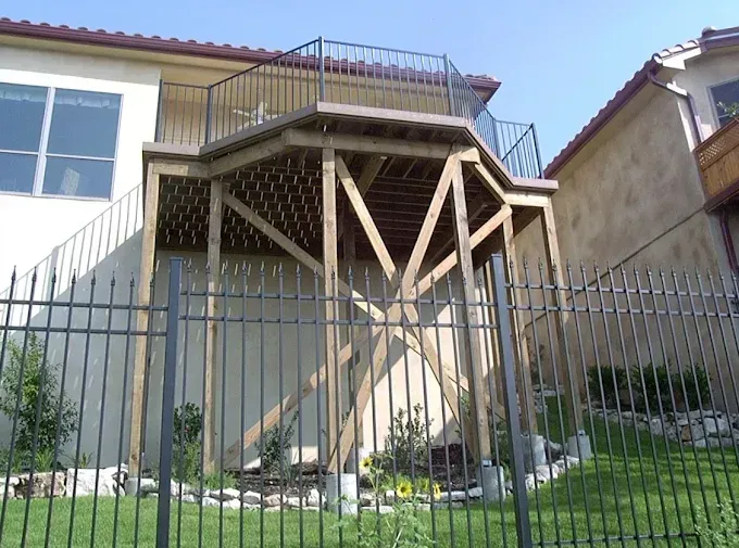 Raised wooden deck with stairs above a fenced yard beside a house