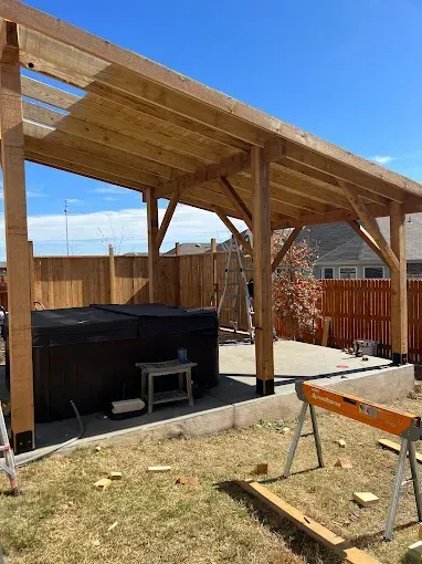 Backyard patio with wooden pergola, hot tub, and sawhorses under a blue sky