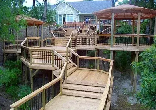 Wooden outdoor deck walkways and gazebos in a lush garden, leading to a house in the background