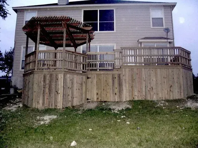 Wooden deck and pergola on a two-story house with a raised retaining wall.