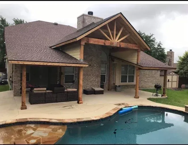 Patio with covered seating area beside a backyard swimming pool and brick house