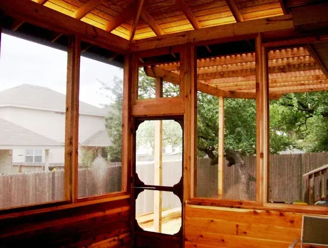 Wooden screened porch with vaulted ceiling, overlooking a fenced backyard and neighboring house.