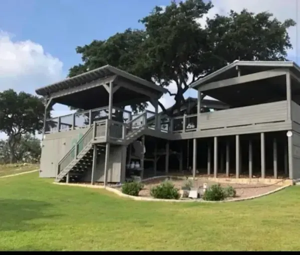 Gray elevated pavilion beside grassy lawn under trees on a sunny day