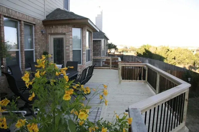 Outdoor wooden deck with black chairs, yellow flowers, and a railing beside a house at sunset