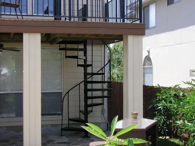 Outdoor apartment patio with spiral staircase, white wall, and small table with potted plant.