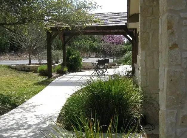 Stone walkway beside a landscaped garden and pergola next to a beige building