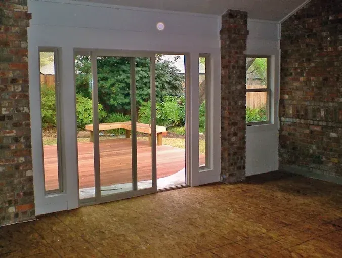Empty room with sliding glass doors, brick accents, and a view of a patio and trees