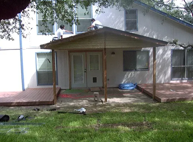 House with a covered front porch and wooden deck, seen from the yard with a person on the roof.