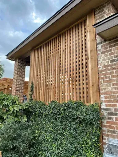 Exterior brick wall with a tall wooden slatted screen and ivy-covered hedge below