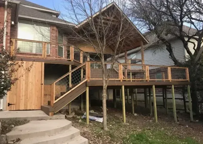 Wooden elevated deck with stairs and railing beside a house, with leafless trees in the yard
