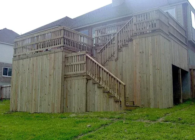 Wooden outdoor deck structure with stairs and railings beside a grassy yard