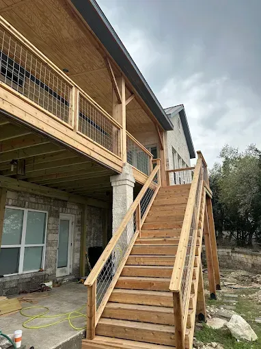 Wooden outdoor staircase with railings leading to a second-floor deck on a house under construction