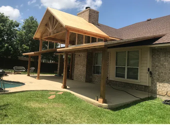Back patio with a wooden pergola, brick house, and green lawn under a sunny sky