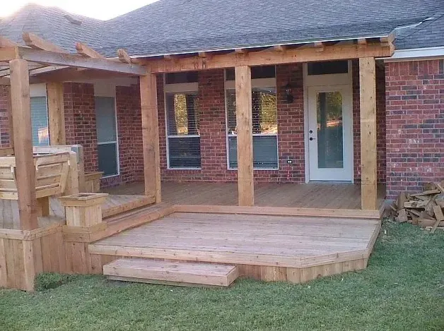 Wooden backyard deck with steps and railing attached to a brick house with a white door