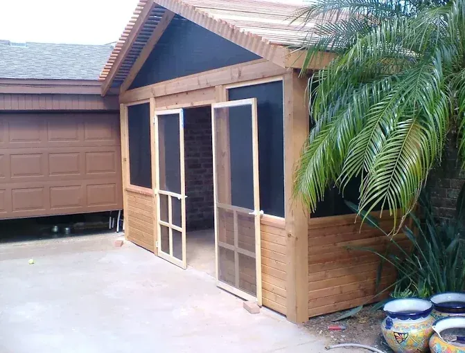 Screened porch with tan wood siding, white-framed doors, garage, and potted plants beside a driveway