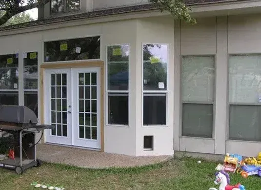 Back patio with white French doors, windows, and a grill beside a grassy yard