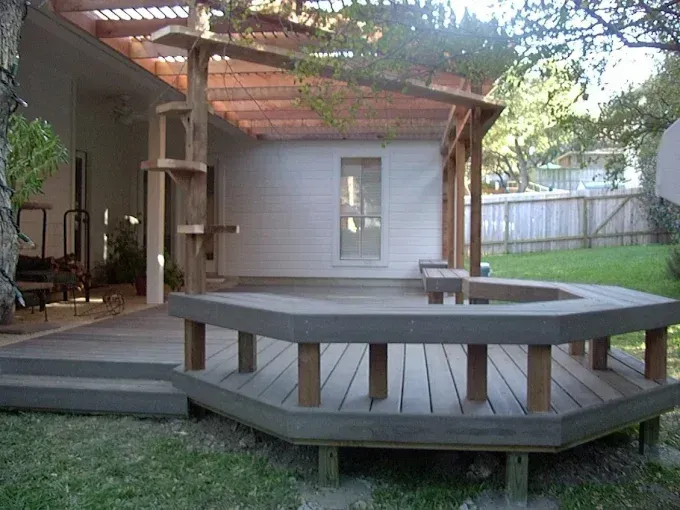 Backyard patio with wooden pergola, deck, and hexagonal seating platform around a fire pit.