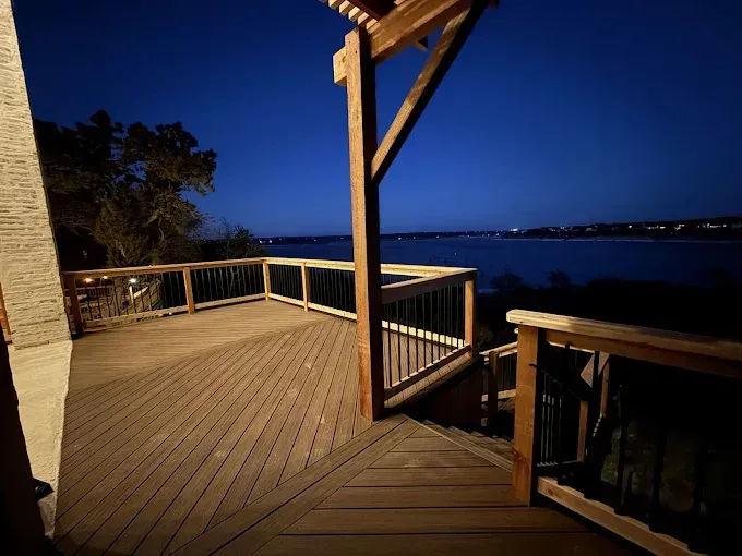 Wooden deck overlooking a calm body of water at dusk, with warm lights and a blue evening sky.