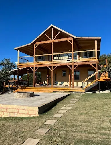 Two-story wooden lodge with wraparound porches, exterior stairs, and a grassy yard under a blue sky