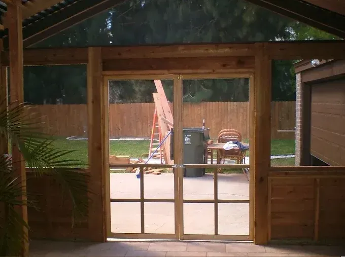 Wood-framed porch looking out to a backyard with a fence, ladder, grill, and patio chairs.