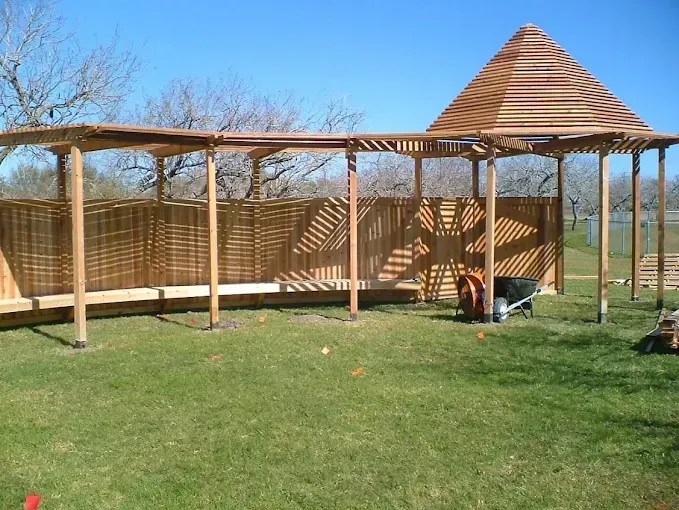 Wooden gazebo with a conical roof on a grassy lawn, with benches and open sides
