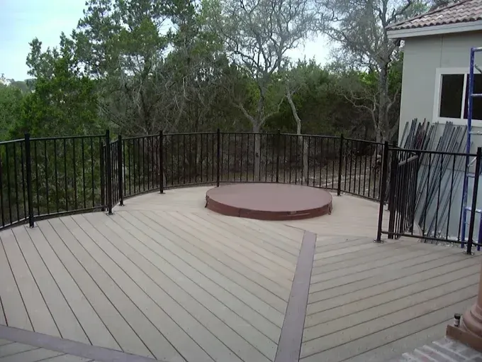 Outdoor deck with black railings, a round wooden platform, and trees in the background