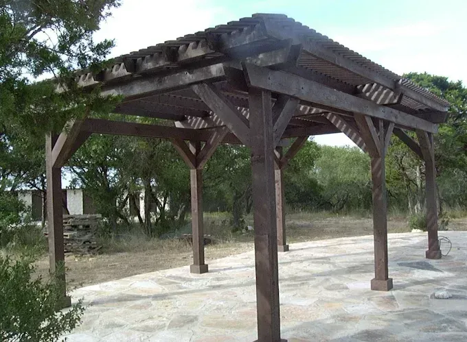 Wooden pavilion with a dark roof on a concrete pad in a sparse outdoor area