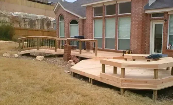 Wooden deck and ramp beside a brick house with large windows and a grassy yard