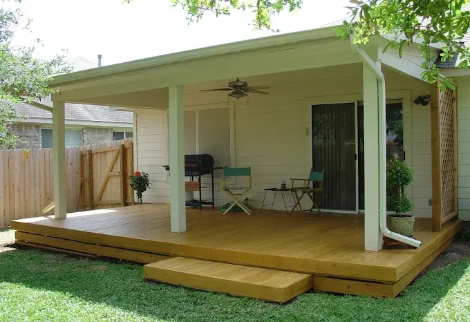 Covered wooden deck with steps, patio chairs, and a ceiling fan in a backyard.