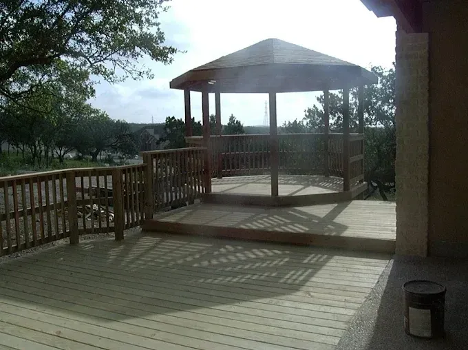 Wooden gazebo on a deck with railings, overlooking trees on a sunny day